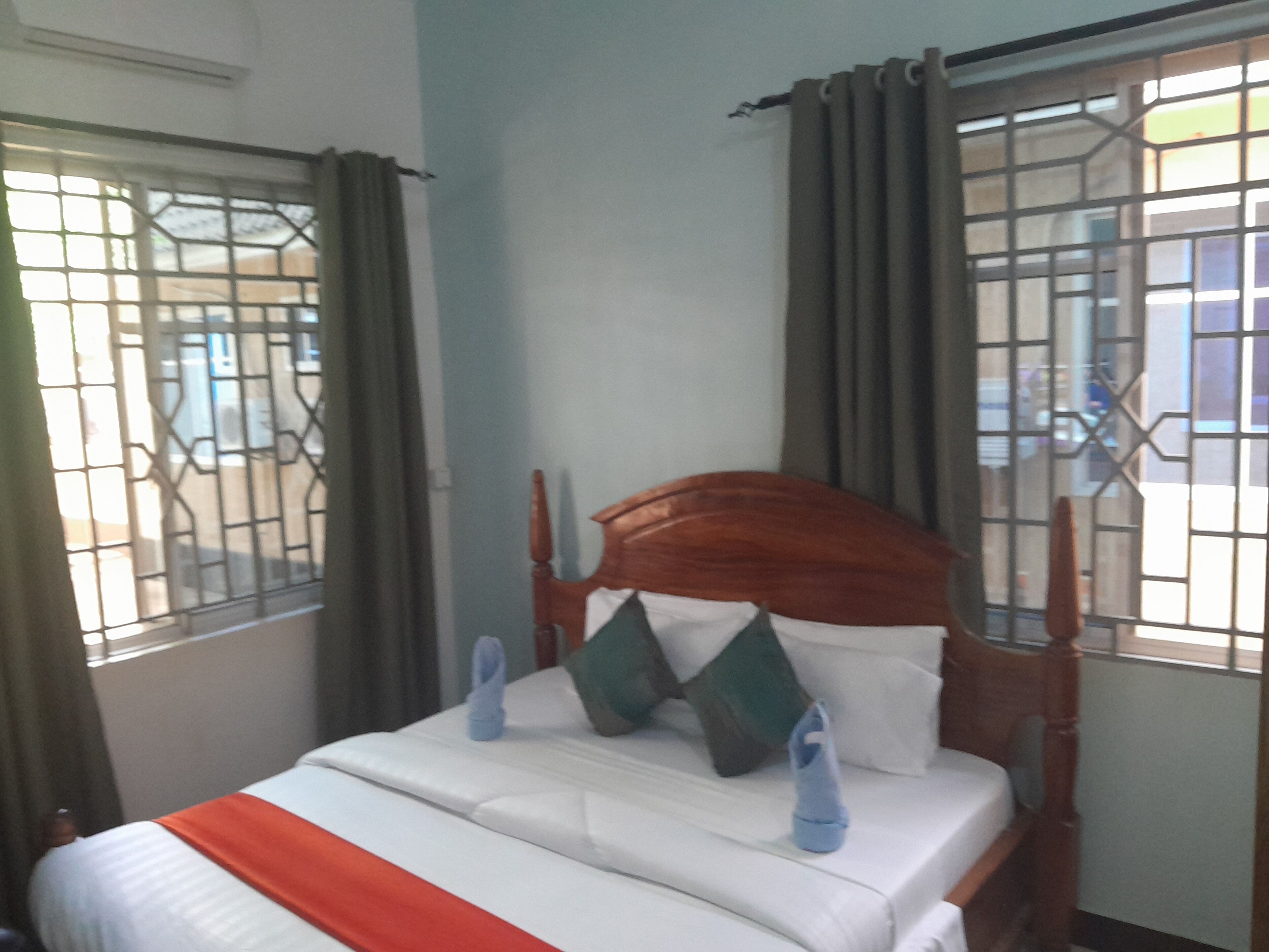 A bed with a wooden headboard, white bedding, and blue slippers.