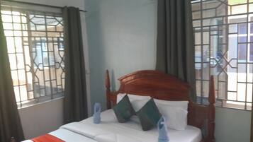 Una cama con cabecera de madera, ropa de cama blanca y pantuflas azules.