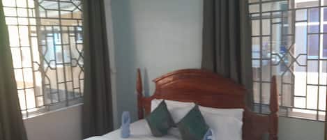 A bed with a wooden headboard, white bedding, and blue slippers.