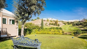 A grassy area with a bench, a tree, and a view of a hill with buildings. - Gh-modern 2 bed Apartment With Pool in Estepona (Estepona)