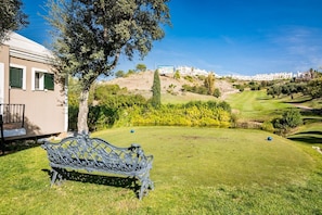 A grassy area with a bench, a tree, and a view of a hill with buildings. - Gh-modern 2 bed Apartment With Pool in Estepona (Estepona)
