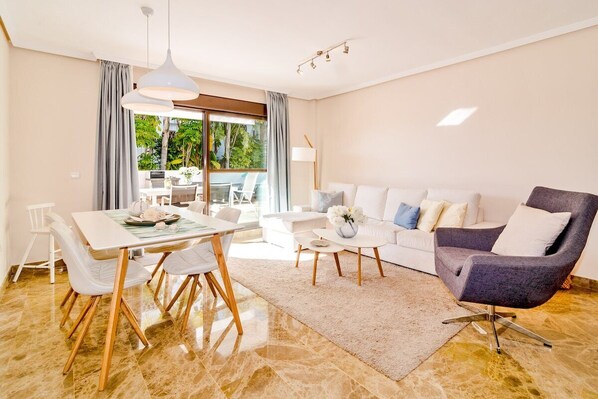 Un salon moderne avec un coin repas, des meubles blancs et une vue sur l’extérieur.