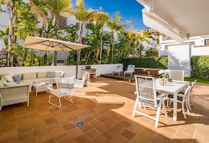 En udendørs terrasse med sofa, stole, et bord og en parasol.