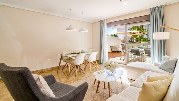 A modern living room with a grey armchair, a white sofa, and a dining area with a table and chairs. - Gh-modern 2 bed Apartment With Pool in Estepona (Estepona)
