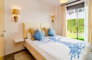 Une chambre à coucher avec un lit, deux lampes fixées au mur, une fenêtre avec des rideaux et une vue sur la verdure à l’extérieur.