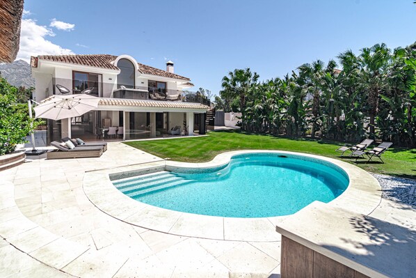 Una casa moderna con piscina, patio coperto e prato curato.