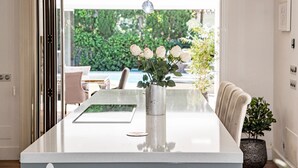 A modern dining area with a white table, a vase of white roses, and a view of a lush garden. - Villa Nottingham Stunning Private Villa (Marbella)