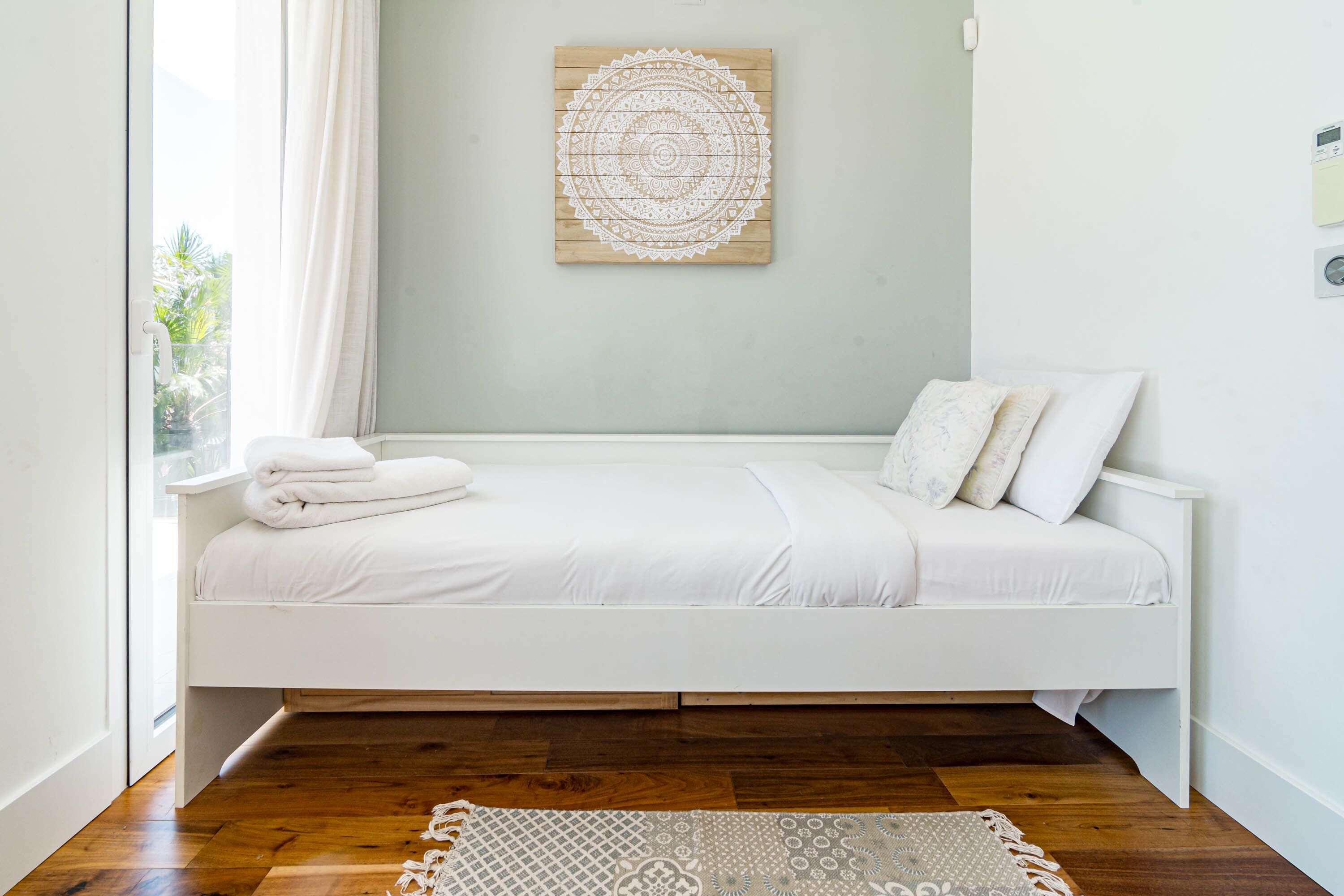 Une chambre à coucher au style minimaliste, avec un lit blanc, un plancher en bois et un élément décoratif circulaire fixé au mur.