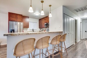 A modern kitchen with wooden cabinets, stainless steel appliances, and a marble countertop. There are three wicker bar stools and pendant lights above the counter. - Relax Fireside: Family Home 6 Mi to Dtwn Beaufort! (Beaufort)
