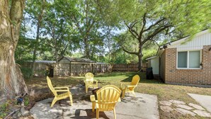 Un patio trasero con suelo de hormigón, cuatro sillas Adirondack, cerca de madera y una casa de ladrillo.