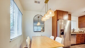 Una cocina moderna con una mesa de comedor de madera, sillas blancas, un refrigerador de acero inoxidable y armarios de madera.