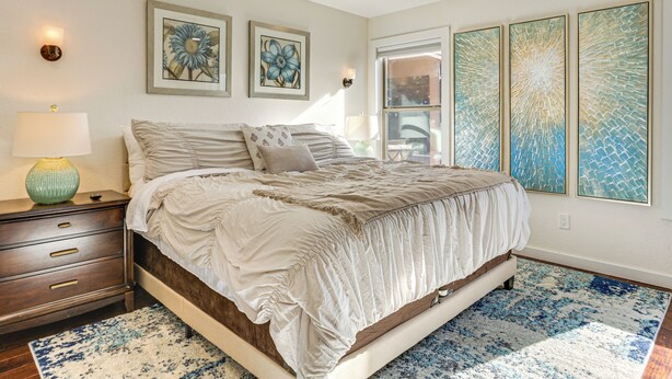 Un dormitorio con una cama grande, una mesita de noche, una lámpara y obras de arte en las paredes.