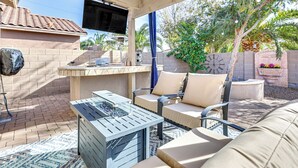 Un patio con mobiliario exterior, un televisor montado en la pared y un reloj.