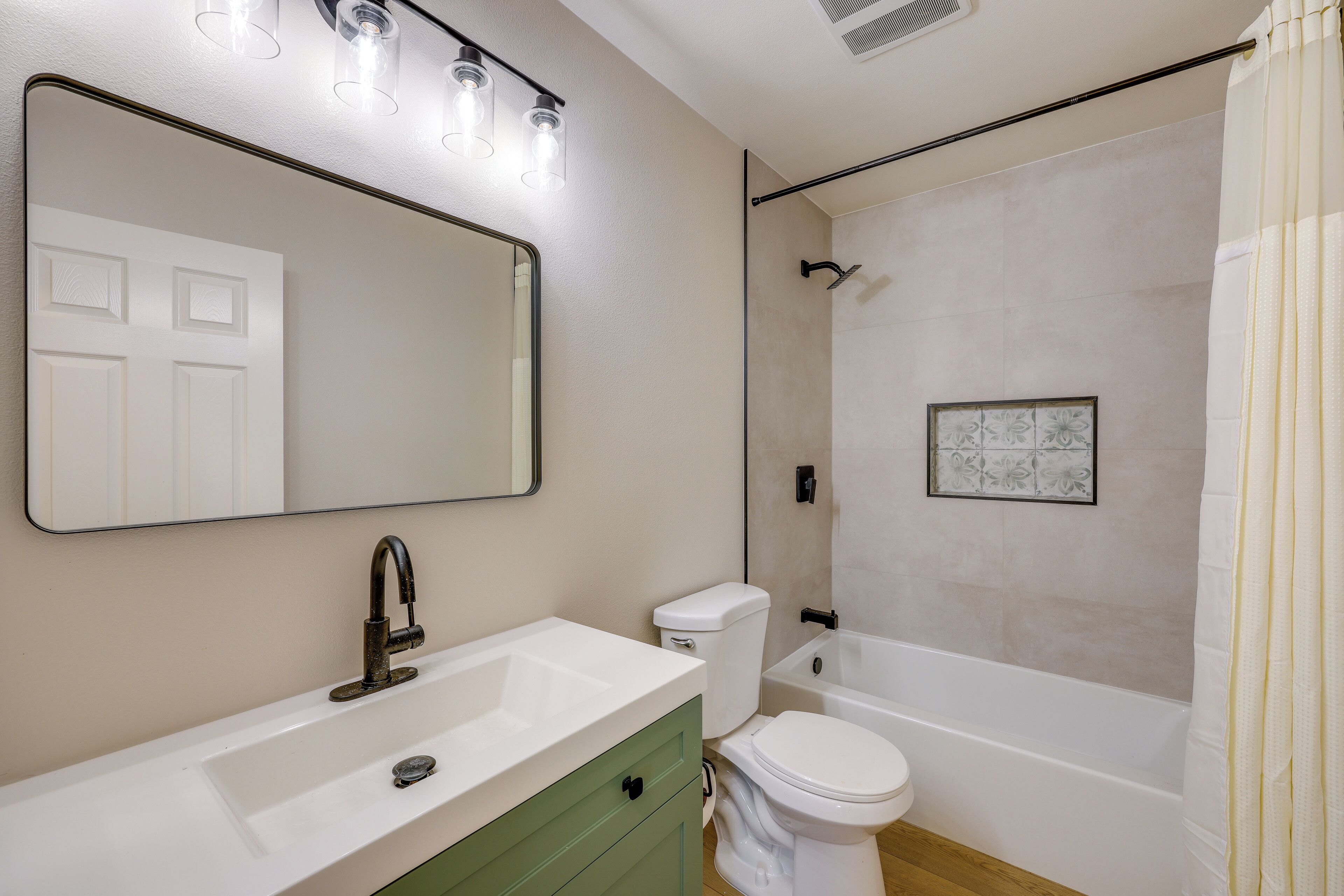 Une salle de bain avec un lavabo blanc, un meuble vert, des toilettes blanches et une baignoire.