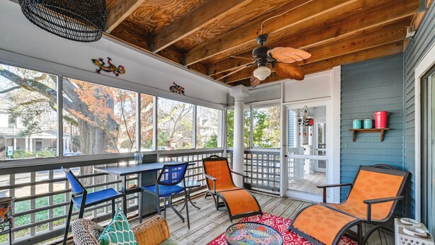 Une véranda couverte avec un plancher en bois, un ventilateur de plafond et une table avec des chaises.