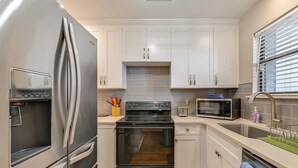 Une cuisine moderne dotée d’appareils électroménagers en acier inoxydable, de meubles blancs et d’un four encastré.