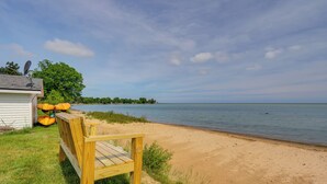 A wooden bench by a sandy beach with a small building and trees in the background. - Waterfront Lake Huron Getaway w/ Private Beach (Port Hope)