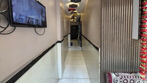 Corredor de hotel com televisão de tela plana na parede, tapete estampado e painel decorativo.