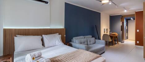 A modern hotel room with a bed, a sofa, a dining table, and a ceiling fan.
