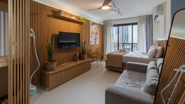 A modern living room with a flat-screen TV, wooden paneling, a sofa, a small table with chairs, and a large window with curtains. - 11 Minutes From the Museum of Tomorrow Vi19 (Rio de Janeiro)