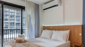 A hotel room with a bed, a wooden headboard, a window with curtains, and an air conditioning unit. - 11 Minutes From the Museum of Tomorrow Vi19 (Rio de Janeiro)