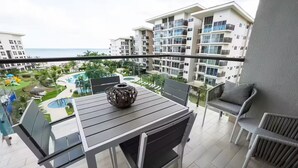 Un balcon avec une table et des chaises, donnant sur une piscine et les bâtiments du complexe hôtelier.