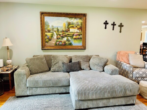 Una sala de estar con un sofá modular, un cuadro de un paisaje y tres cruces colgadas en la pared.