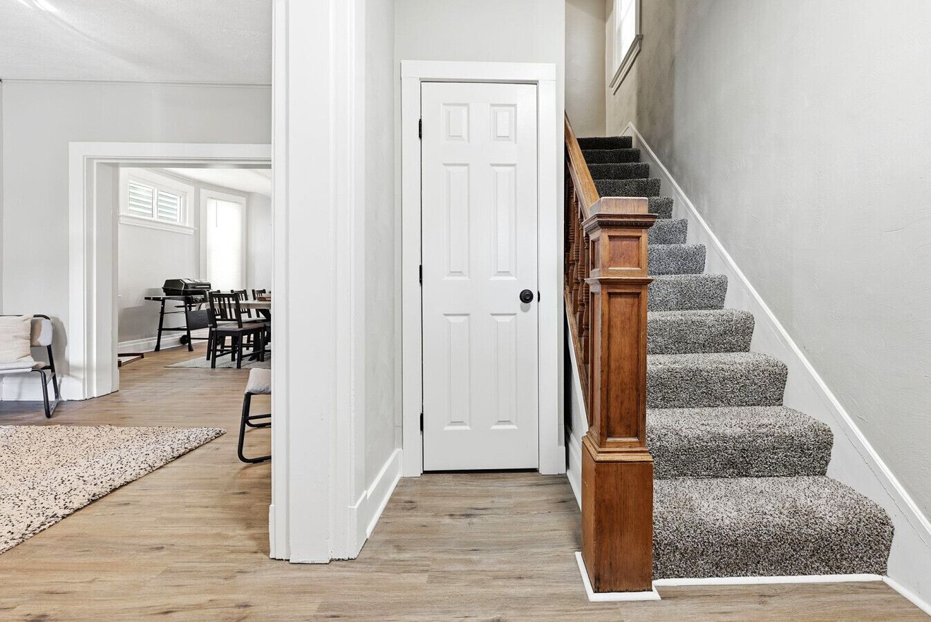 Un couloir avec un escalier en bois, une porte blanche et un coin repas avec des chaises et des tables.