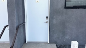 A building entrance with a white door marked with the number 2, a small window above it, and a metal handrail leading to the door. - Quaint, New Hideaway Studio-sized Room (San Diego)