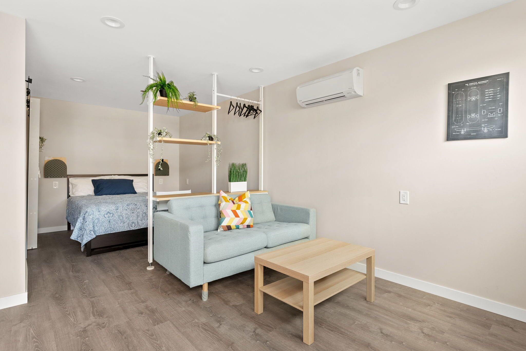 A modern living room with a light blue sofa, a wooden coffee table, and a built-in shelving unit with plants.