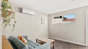 A living room with a grey sofa, a wooden coffee table, and a small side table. There is a window with a view of a building and a plant hanging from the ceiling. - Comfortable New Room in one of San Diego's best Neighborhoods (San Diego)
