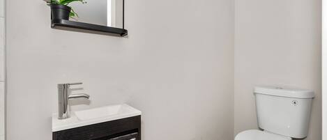 Une salle de bain avec un lavabo blanc, un miroir, des toilettes et une orchidée en pot.