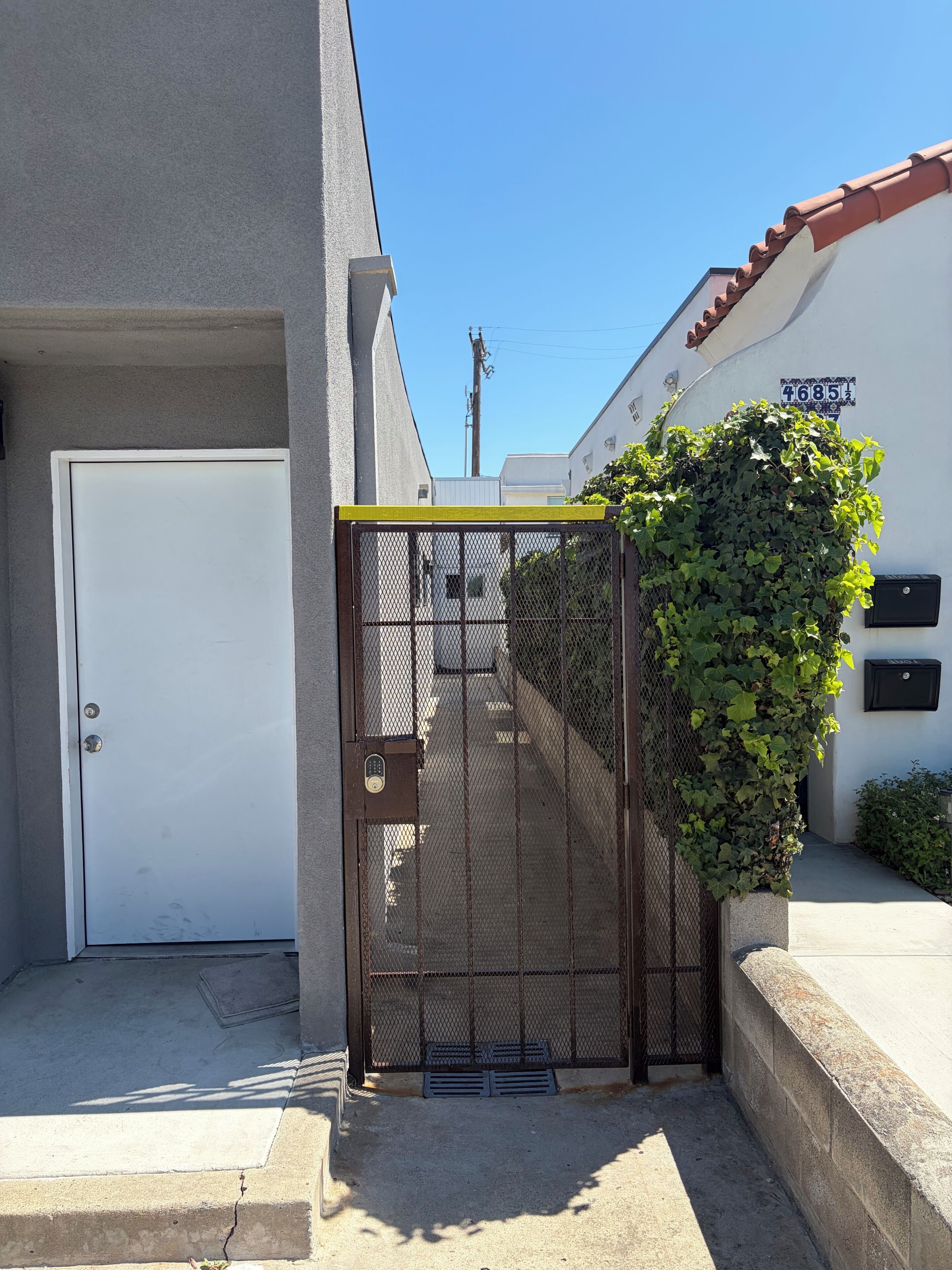 A gated entrance with a metal fence, a white door, and a building with a number sign.