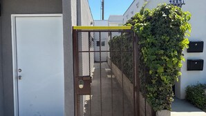 A gated entrance with a metal fence, a white door, and a building with a number sign.