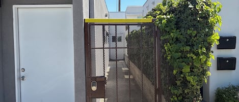 A gated entrance with a metal fence, a white door, and a building with a number sign.