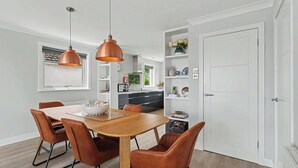 Un espace repas moderne avec une table en bois et des chaises marron, une cuisine en arrière-plan et une porte blanche.