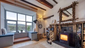 Un salon chaleureux avec une cheminée, une grande fenêtre donnant sur la campagne et un banc intégré agrémenté de coussins.