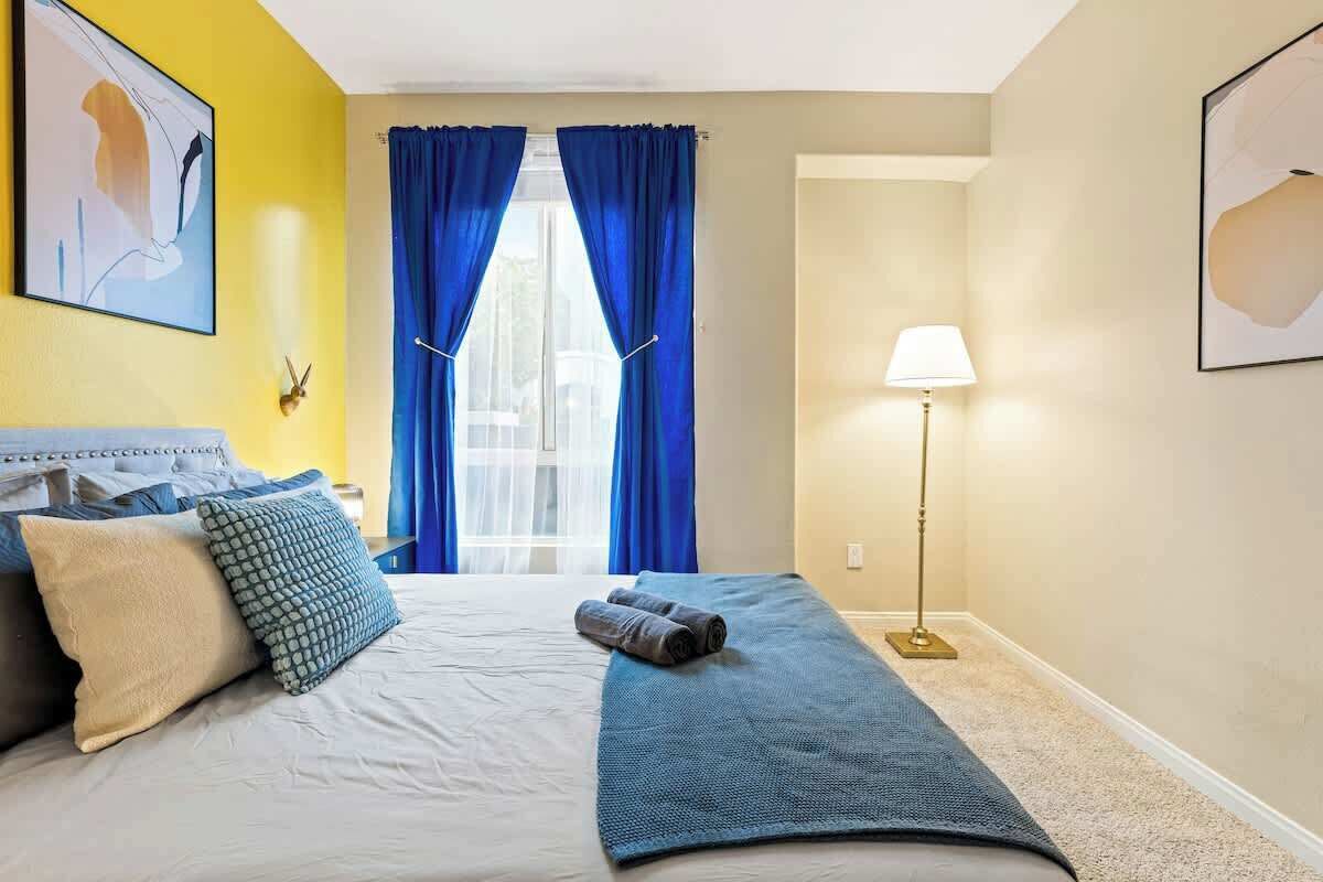 Een hotelkamer met een bed, een blauwe handdoek, een lamp en een raam met blauwe gordijnen.