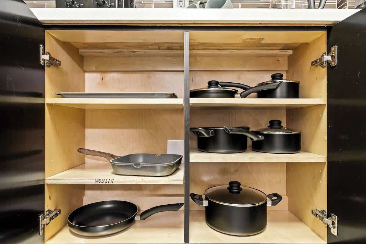 A kitchen cabinet with multiple shelves, each holding different kitchenware like frying pans and pots.