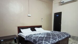 A bedroom with a bed, a bedside table, a wall-mounted air conditioner, and a door. - Brajrani Hotel (Datia)