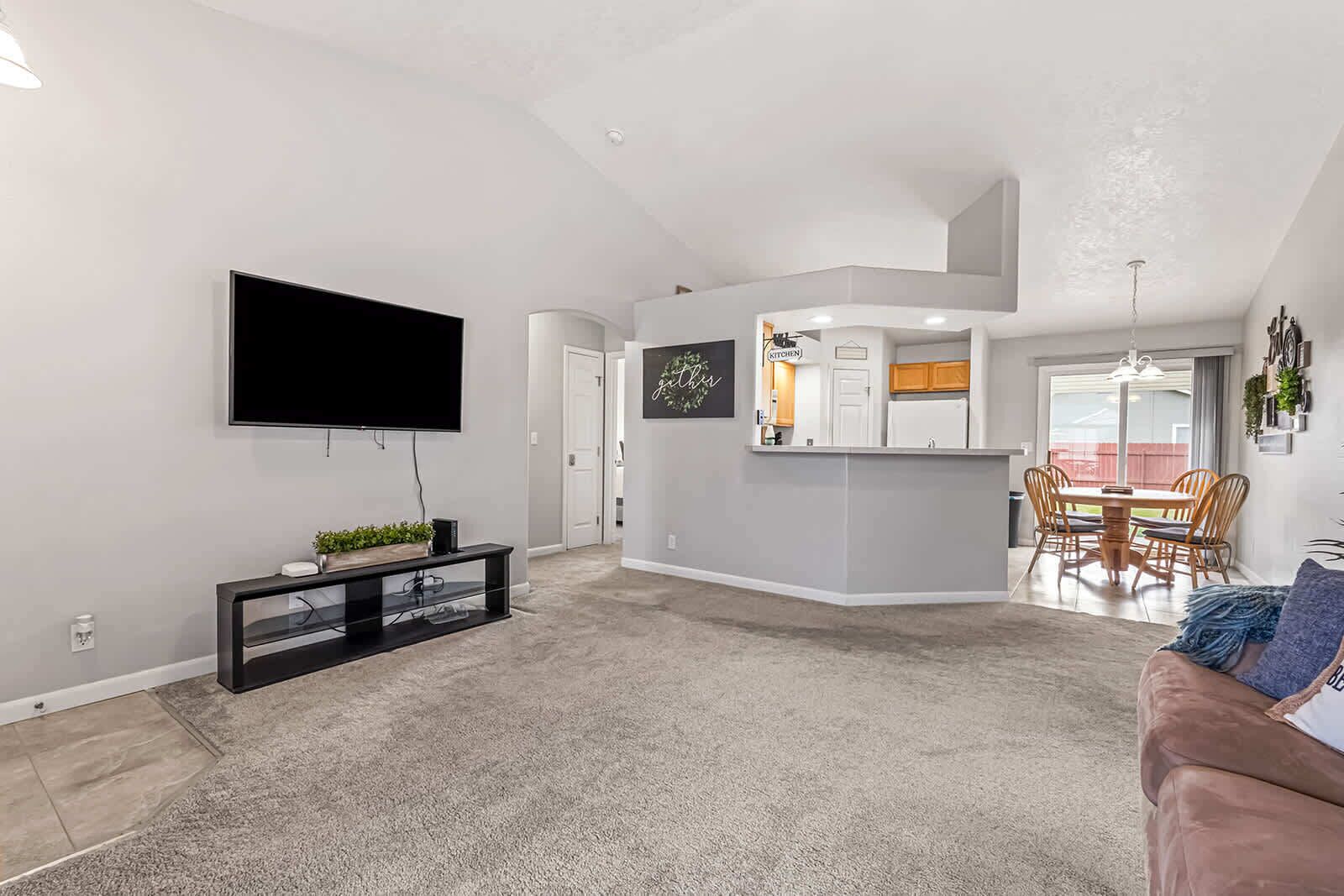 A modern living room with a flat-screen TV, a black entertainment unit, and a beige carpet.