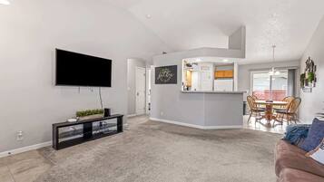 A modern living room with a flat-screen TV, a black entertainment unit, and a beige carpet.