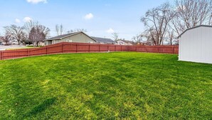 Un jardin bien entretenu, avec une clôture en bois rouge, un abri de jardin blanc et une maison en arrière-plan.
