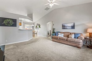 A spacious living room with a high ceiling, a brown leather sofa, and a dining area in the background. - Cozy 3BR Nampa Home • Spacious Yard + Smart TV (Nampa)