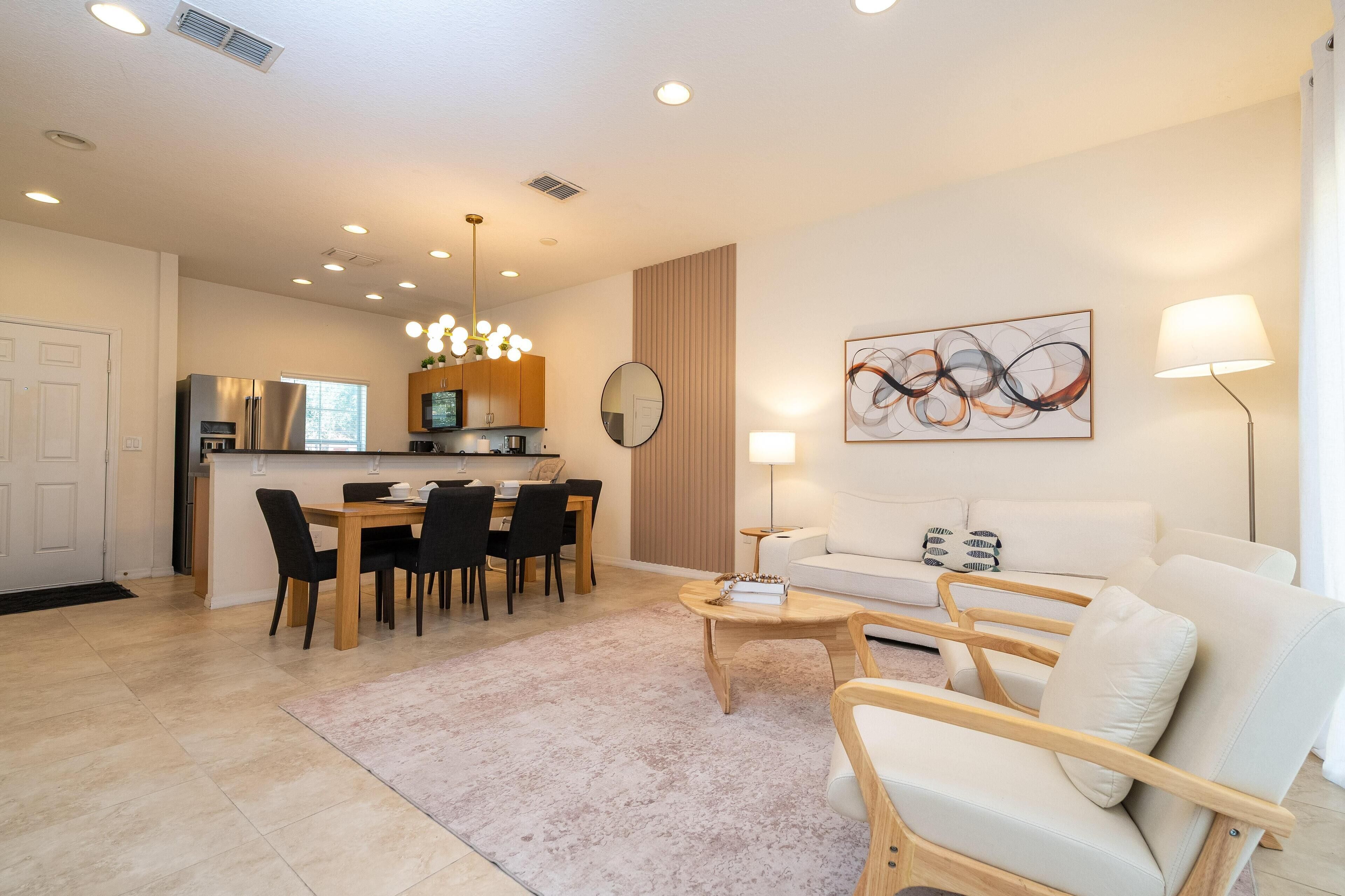 A modern living room with a white sofa, wooden coffee table, and a dining area with a wooden table and chairs.