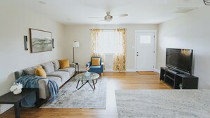 A living room with a sofa, a blue armchair, a glass coffee table, a TV, and a ceiling fan. - Spacious & Stylish– Near Downtown Raleigh (Raleigh)
