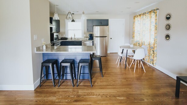 A modern kitchen with a central island, bar stools, a dining area with a table and chairs, and a large window. - Spacious & Stylish– Near Downtown Raleigh (Raleigh)
