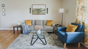 A living room with a grey sofa, a blue armchair, a glass coffee table, and a patterned rug. - Spacious & Stylish– Near Downtown Raleigh (Raleigh)