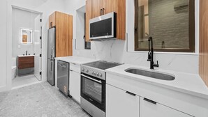 Cozinha moderna com bancadas brancas, armários de madeira, micro-ondas embutido, geladeira de aço inoxidável e forno duplo.