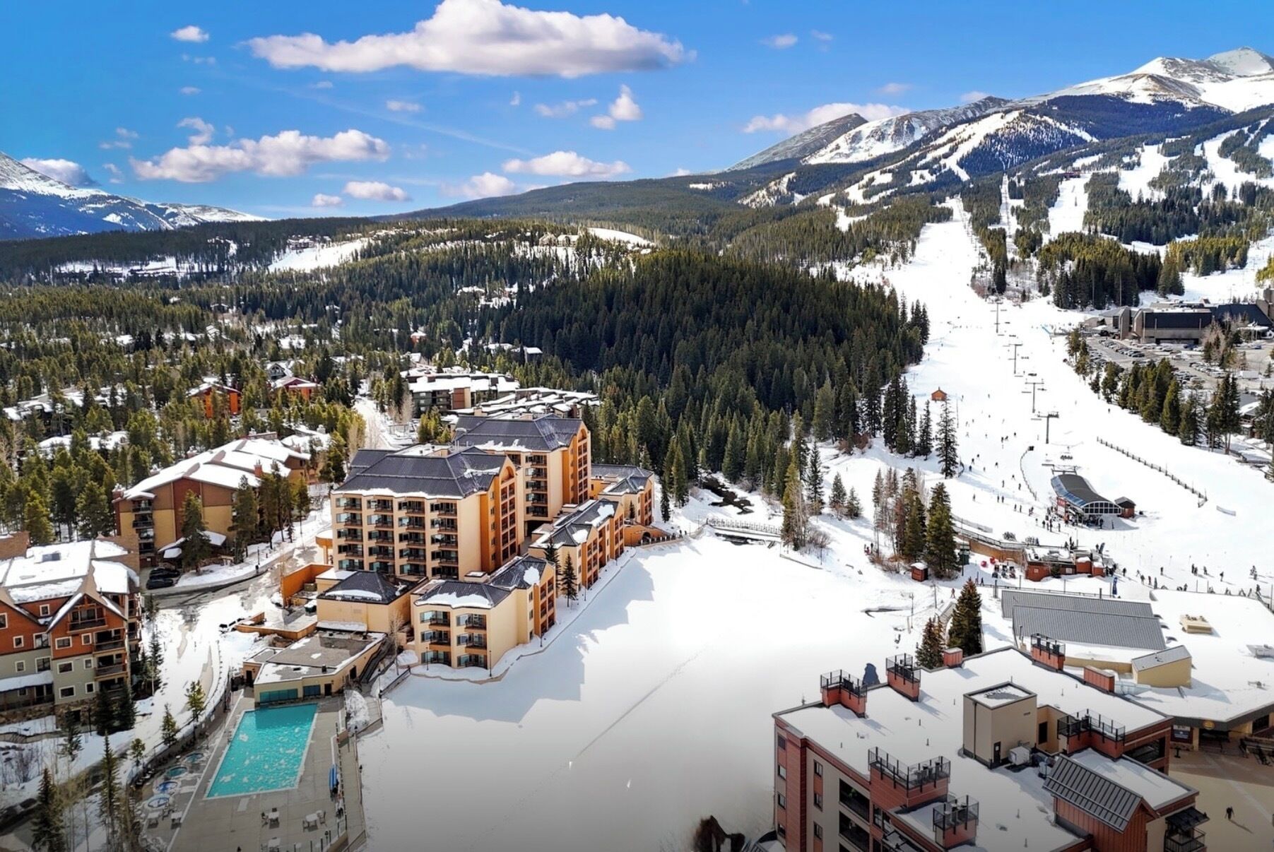 A ski resort with multiple buildings, a swimming pool, and a snow-covered landscape with mountains in the background.